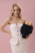 Woman in a white strapless dress holding a black clutch with bread inside on a pink background