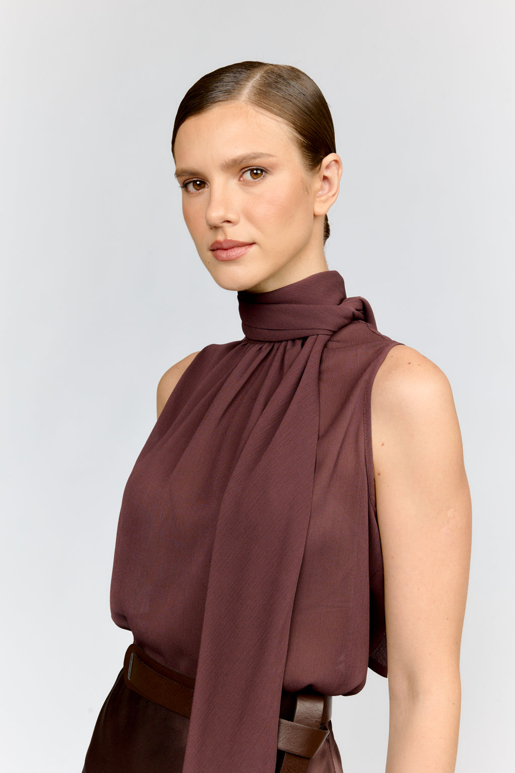 Woman wearing a brown sleeveless top with a high neckline against a light gray background