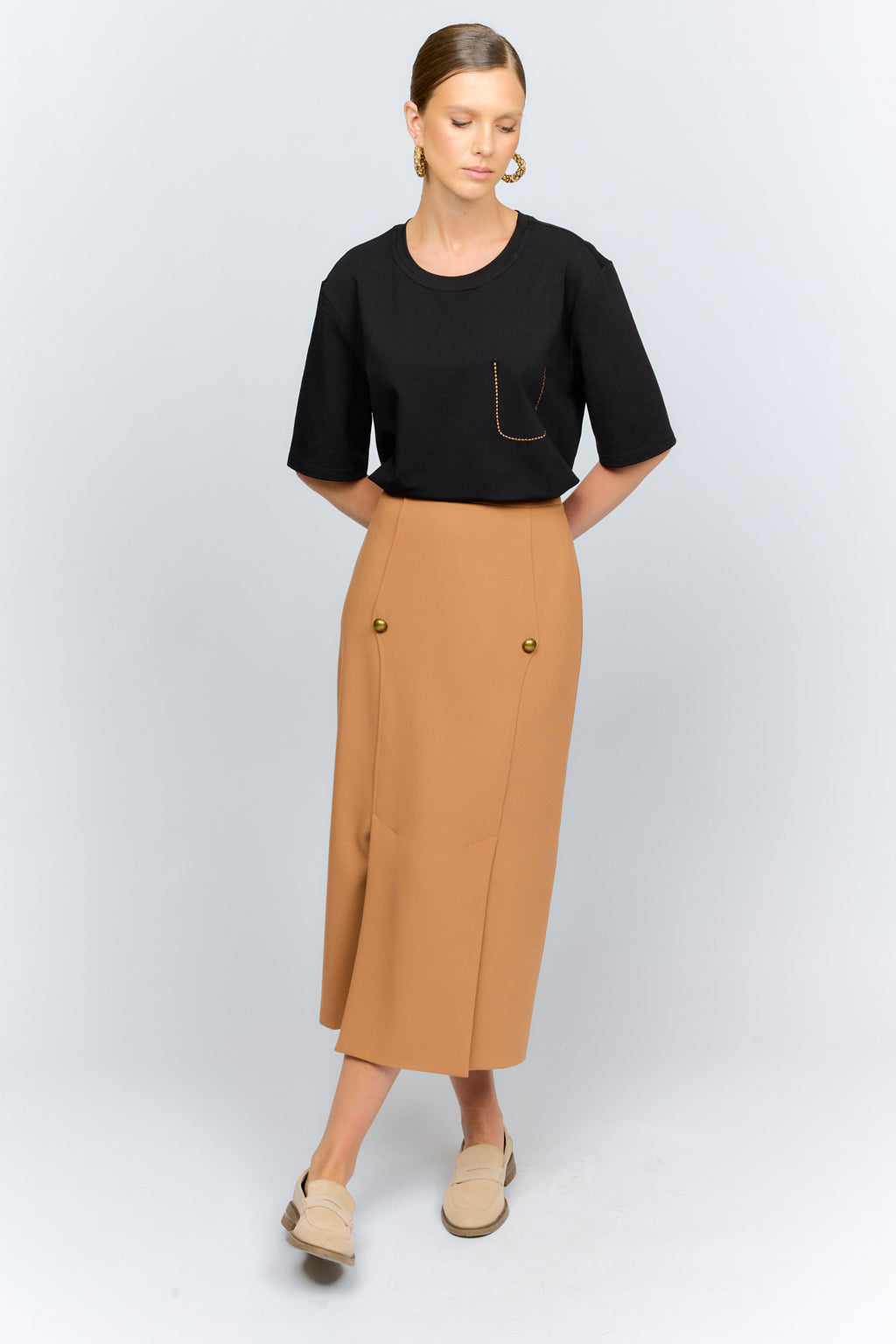 Woman wearing a black top and tan skirt on a white background