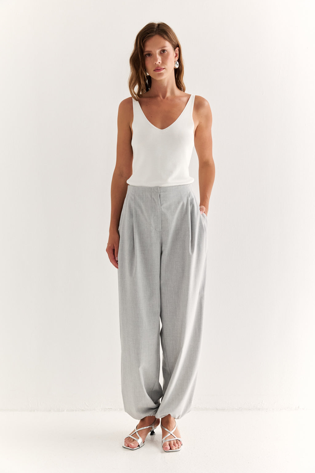 Woman wearing a white tank top and gray pants on a white background