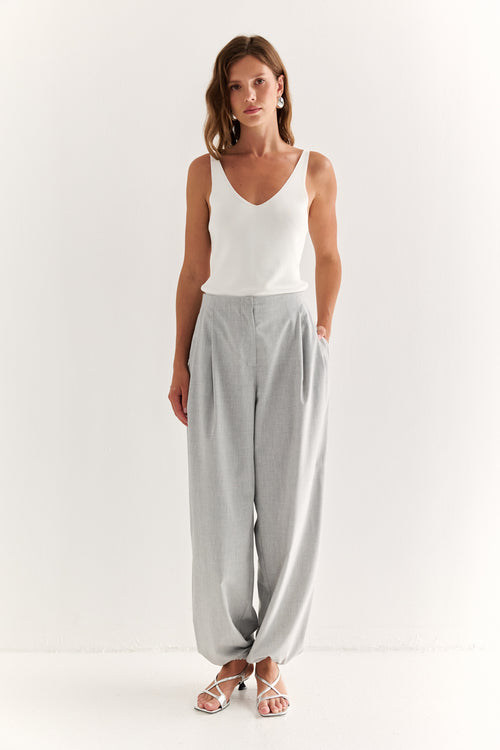 Woman wearing a white tank top and gray pants on a white background