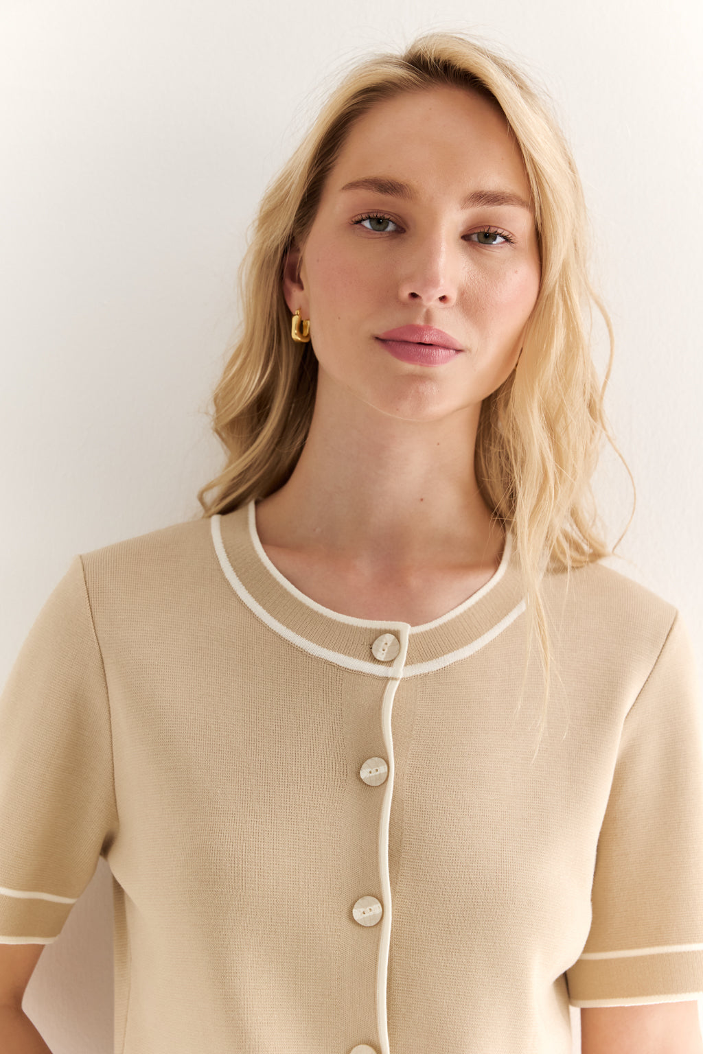 Woman wearing a beige dress with white trim against a plain background