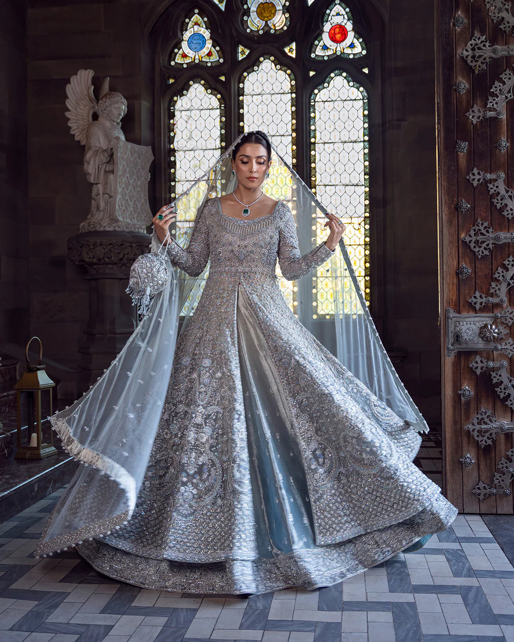 Woman in an elaborate silver gown standing in a cathedral with stained glass windows.