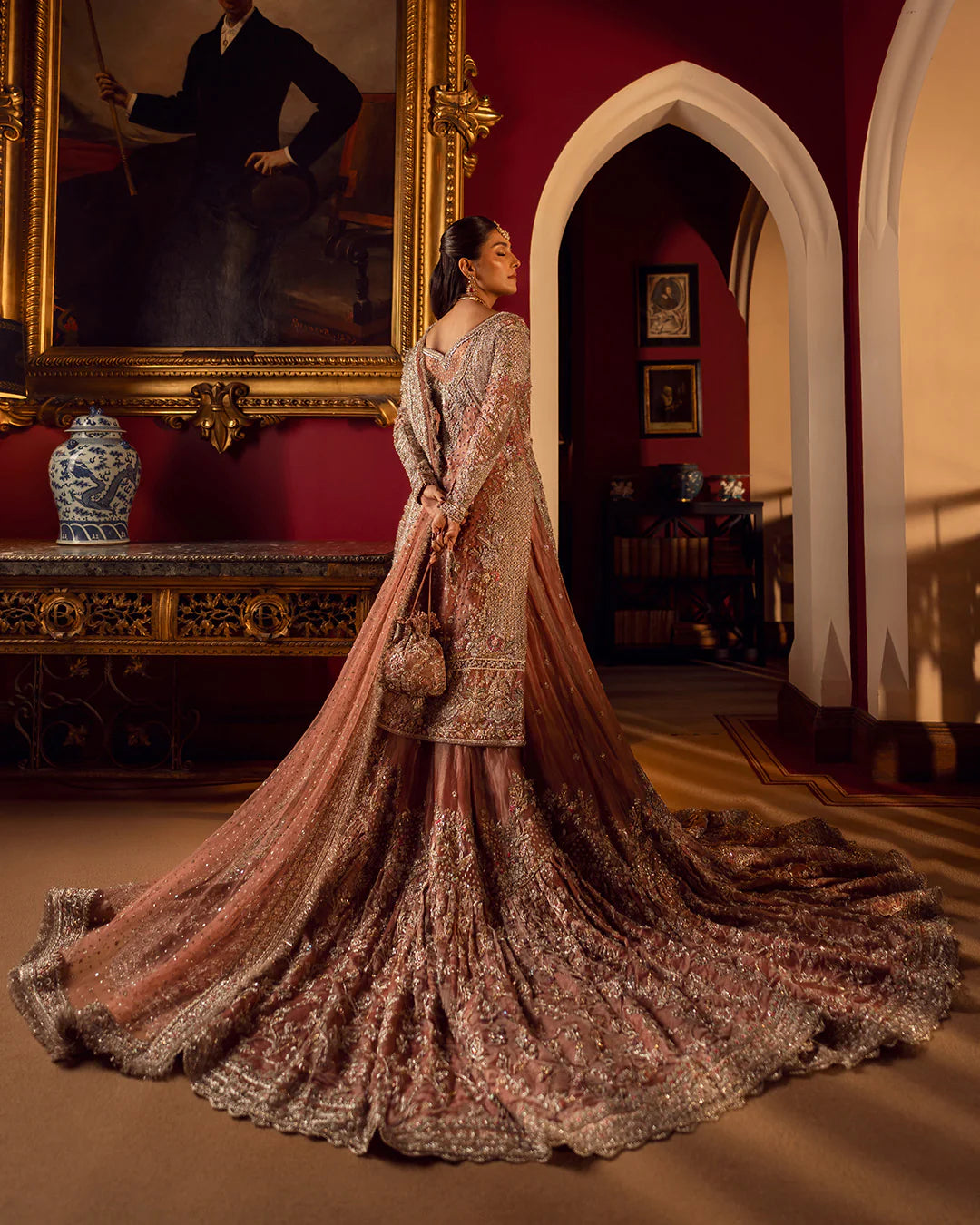 Woman in an ornate dress standing in a room with red walls and a large mirror.