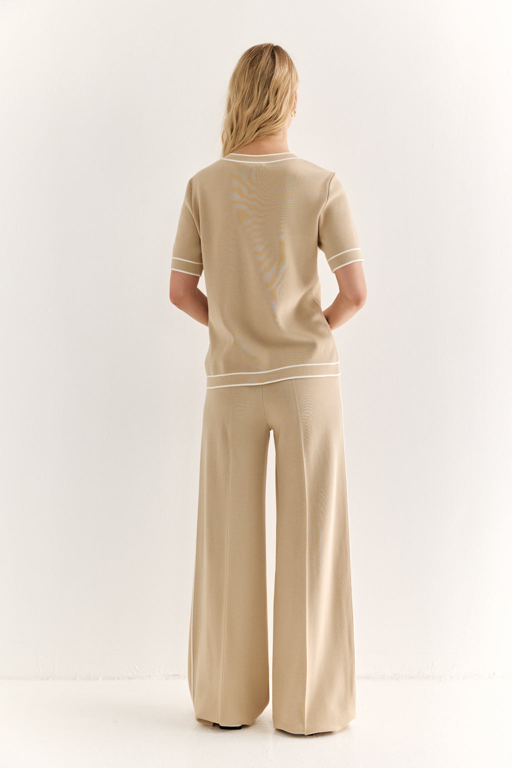 Person wearing a beige outfit with white trim on a white background