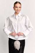 Woman wearing a white blouse with a black skirt and holding a silver clutch against a white background