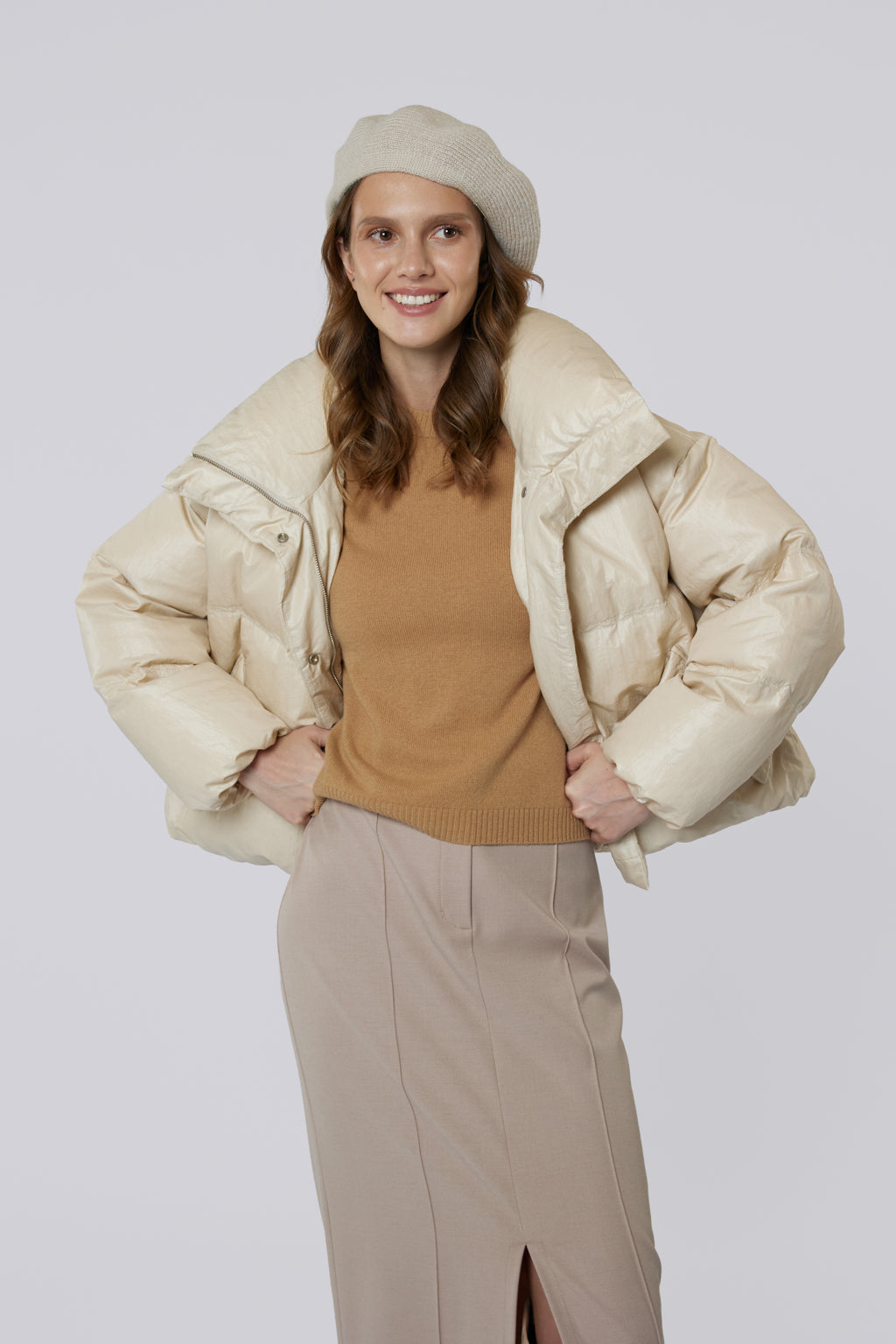Woman wearing a beige puffer jacket, brown top, and beige pants on a white background