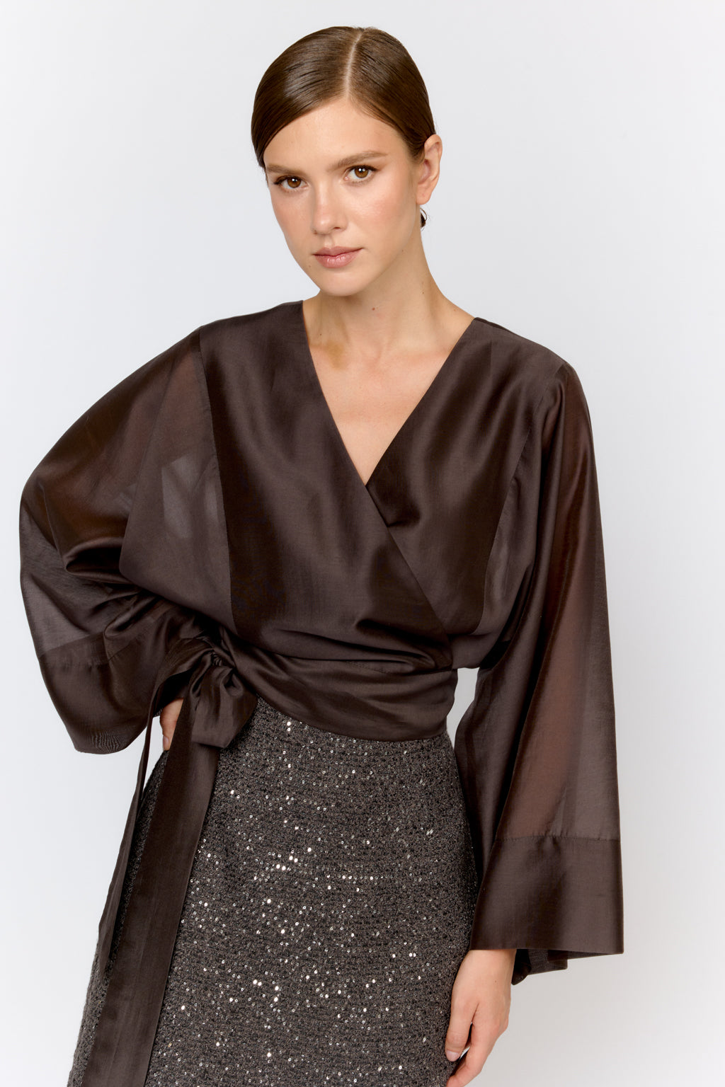 Woman wearing a brown top with wide sleeves and a sequined skirt on a white background