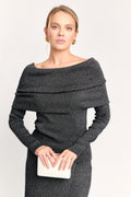 Woman wearing a dark gray off-shoulder dress holding a clutch against a white background