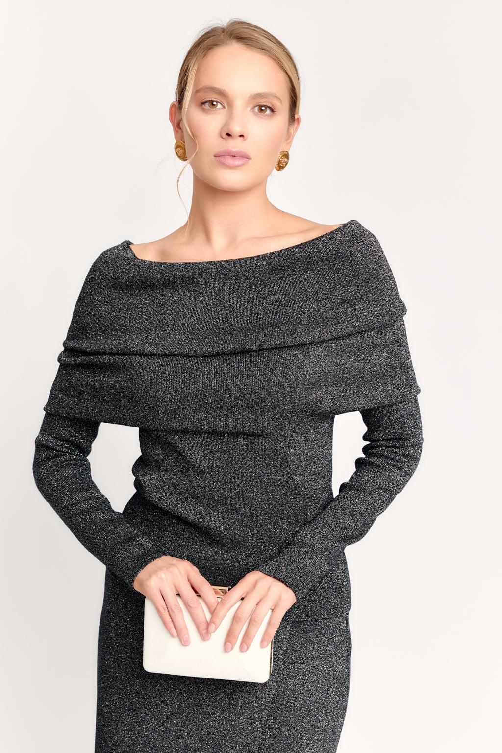 Woman wearing a dark gray off-shoulder dress holding a clutch against a white background