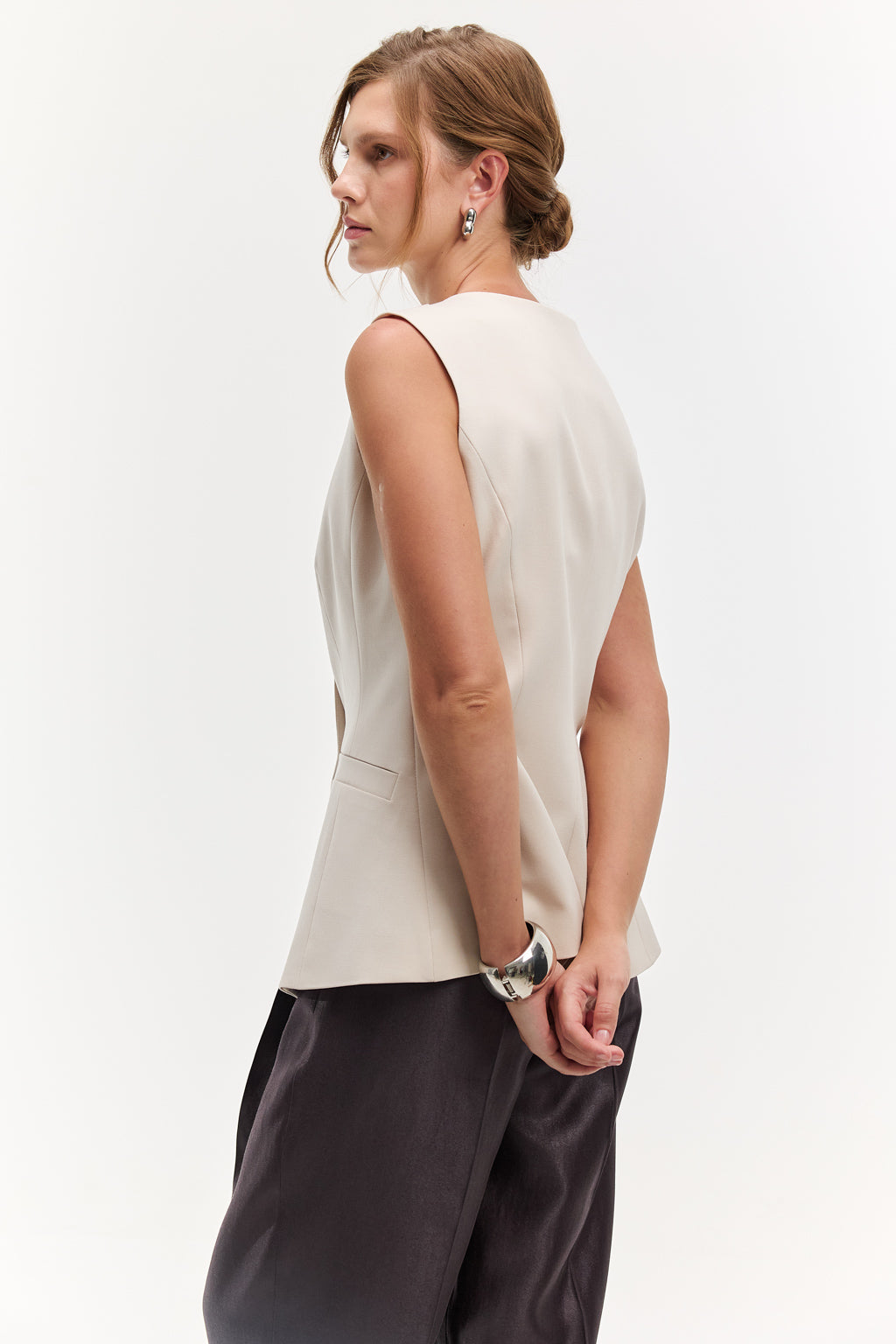 Woman wearing a white sleeveless top and dark pants on a white background