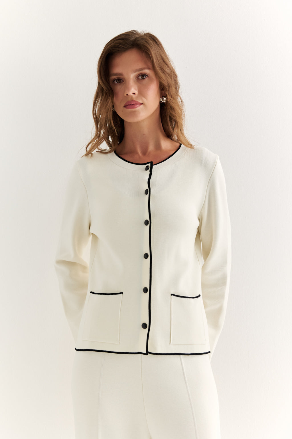 Woman wearing a white cardigan with black trim on a white background