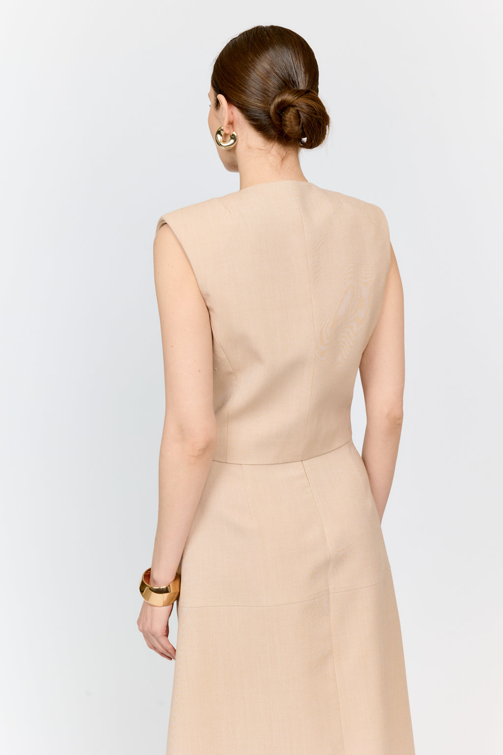 Woman wearing a beige sleeveless dress against a white background