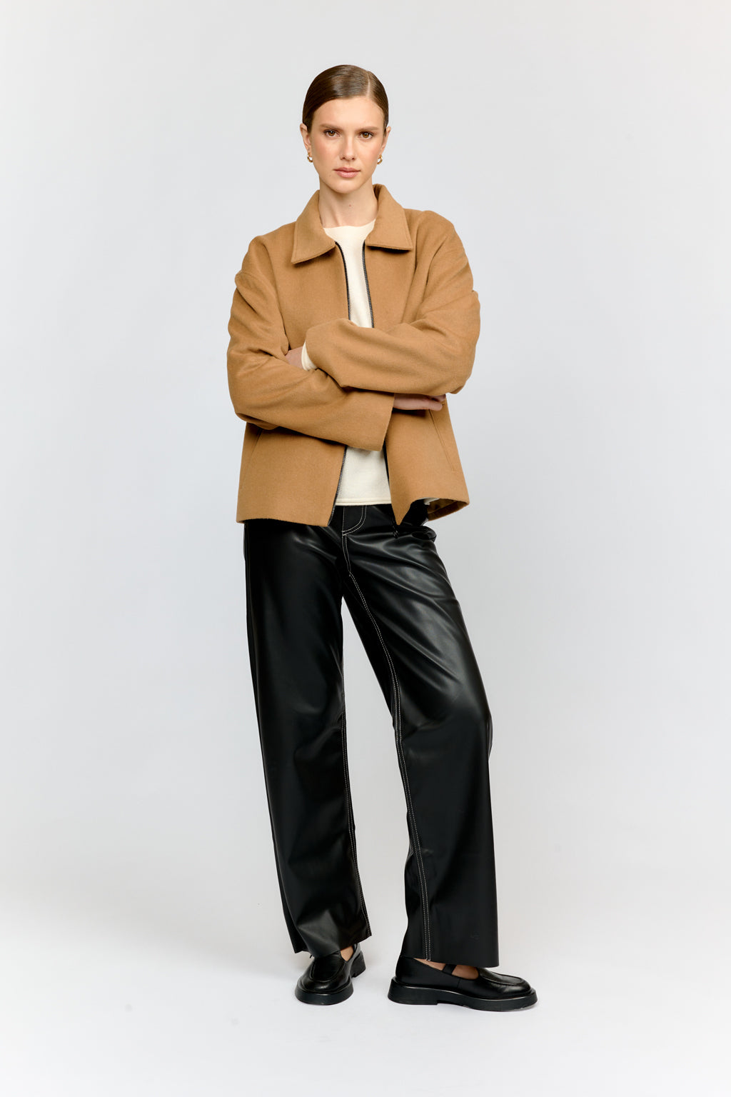 Person wearing a brown coat and black pants on a white background