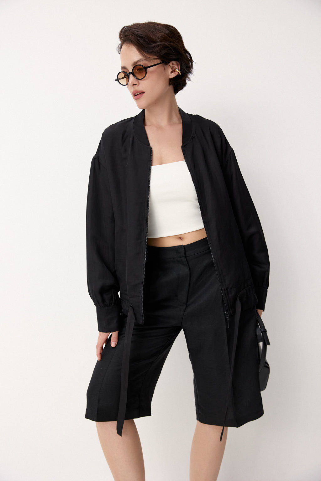 Woman wearing DEITY Midnight Bomber Wrap with white wide-leg trousers and black sunglasses.