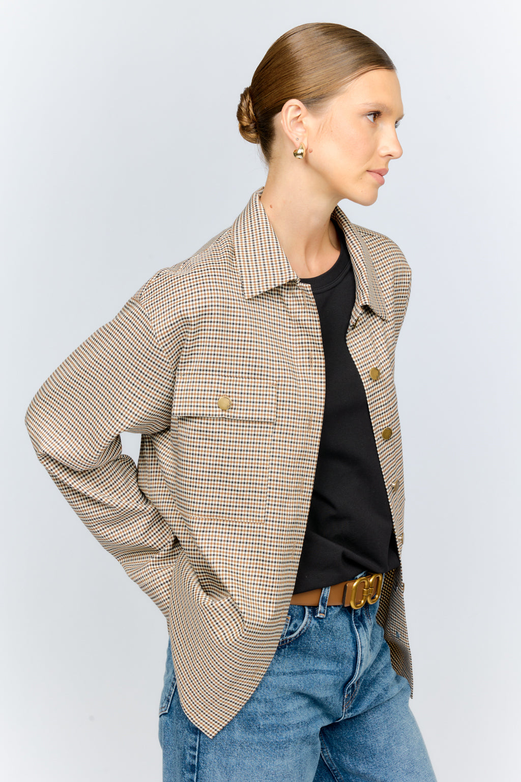Woman wearing a beige checkered blazer over a black top and blue jeans on a light gray background