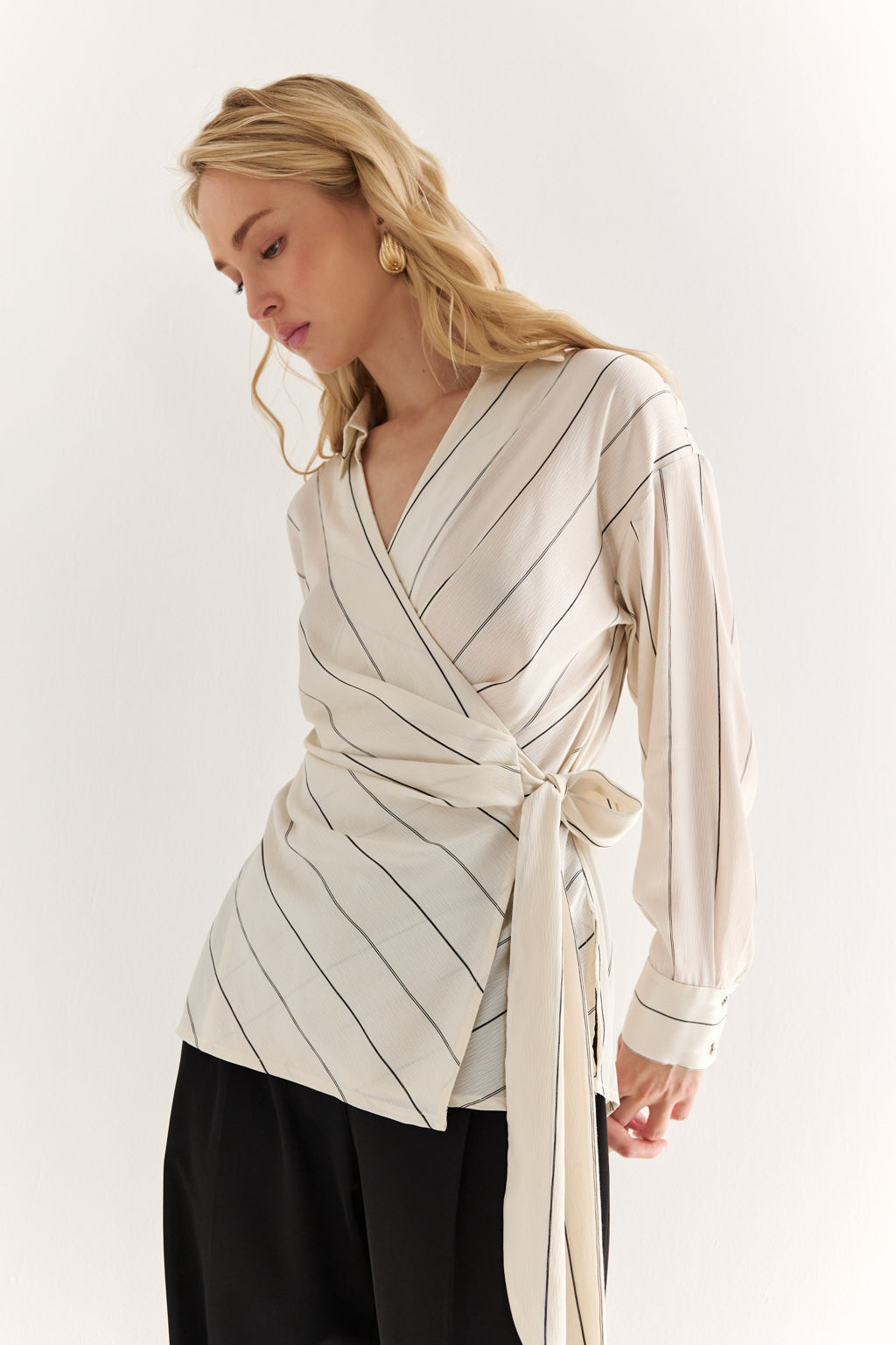 Woman wearing a cream-colored wrap-style blouse with black pants on a white background