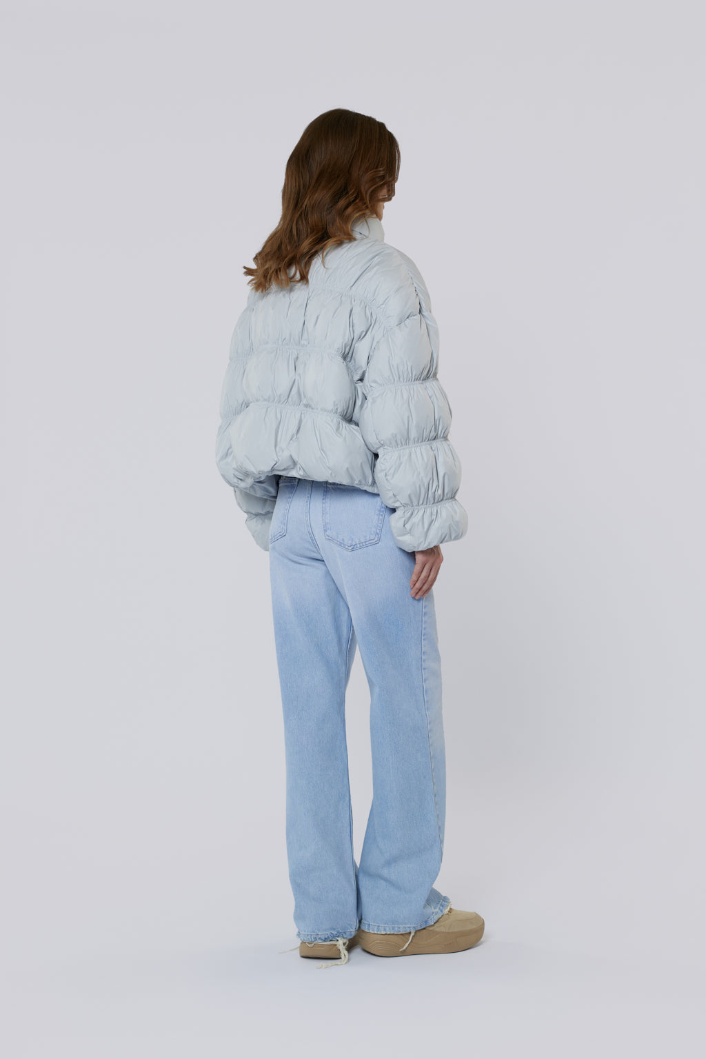 Person wearing a light blue puffer jacket and jeans on a white background