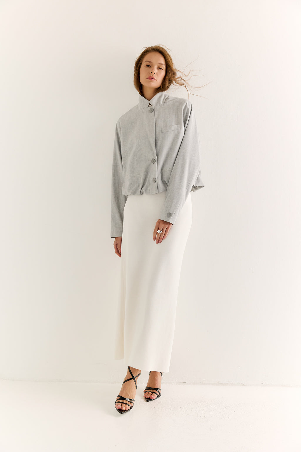 Woman wearing a gray cardigan and white pants on a white background