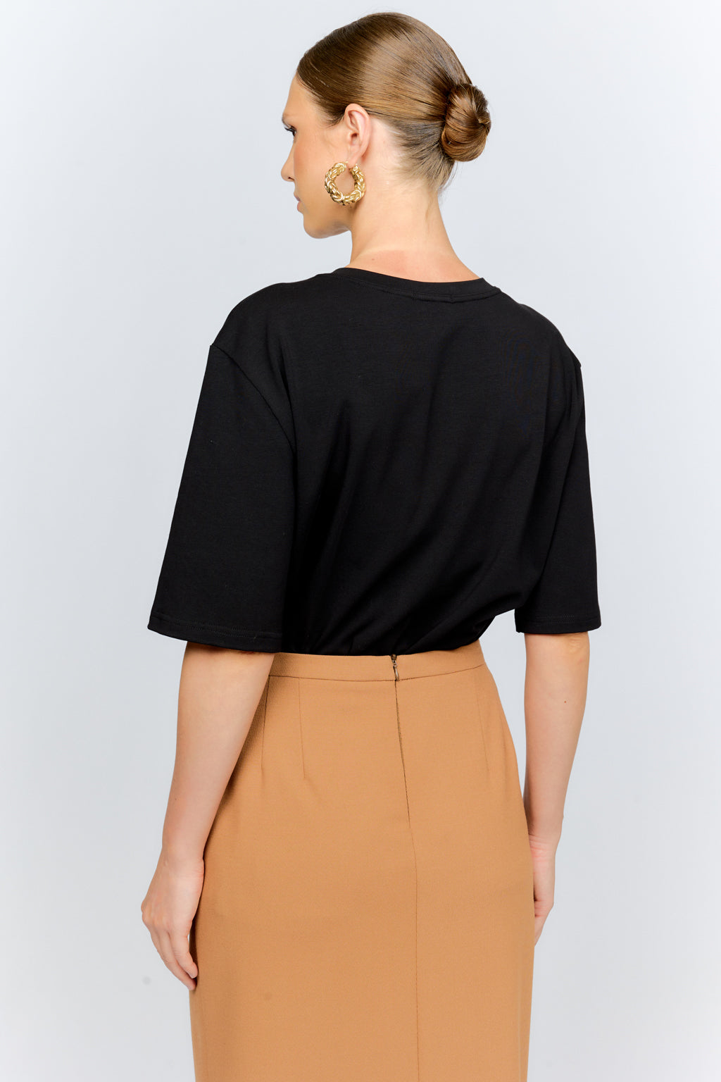 Woman wearing a black top and tan pants on a white background