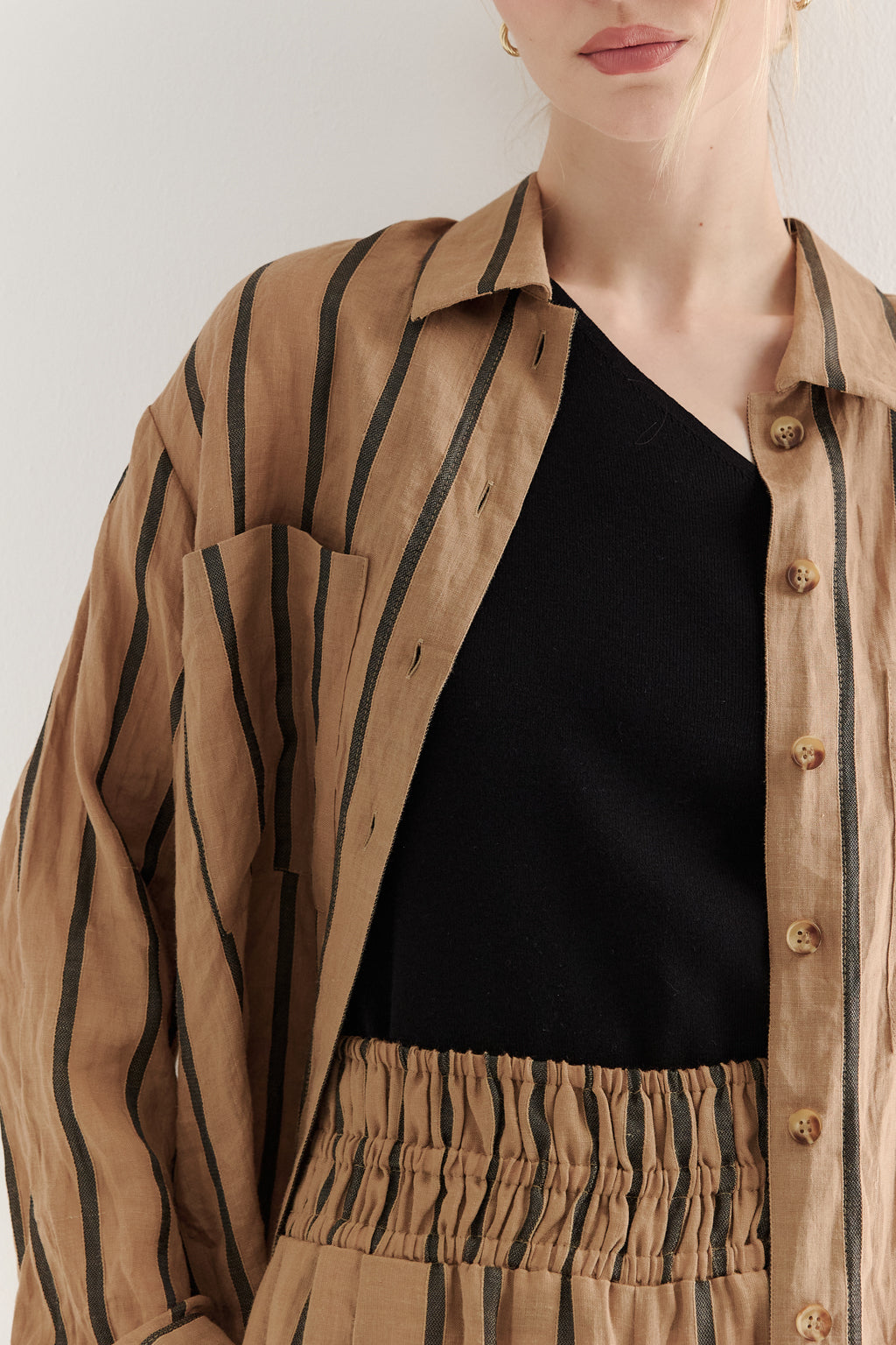 Person wearing a beige striped shirt over a black top with a plain background