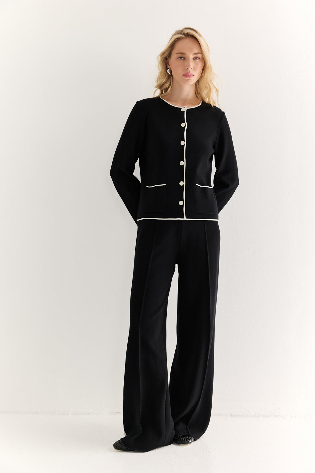 Woman wearing a black outfit with white buttons on a white background