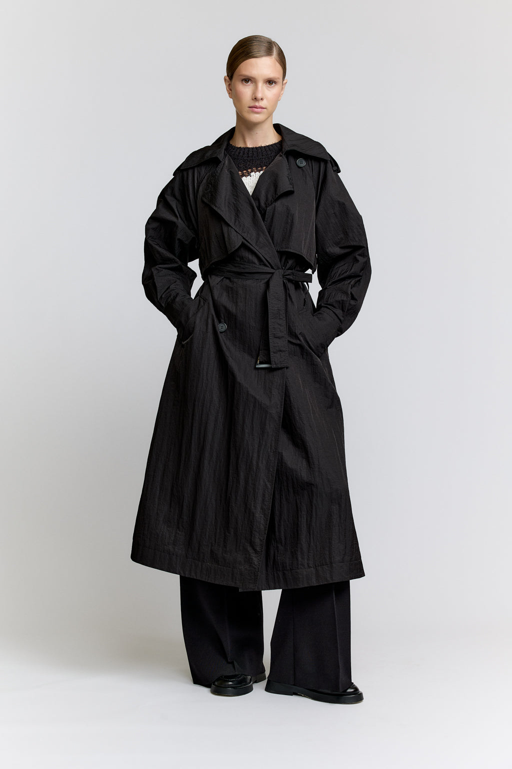 Person wearing a black trench coat on a white background