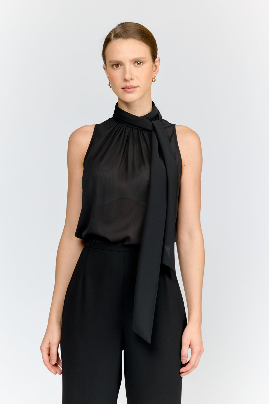 Woman wearing a black sleeveless top with a tie detail on a white background