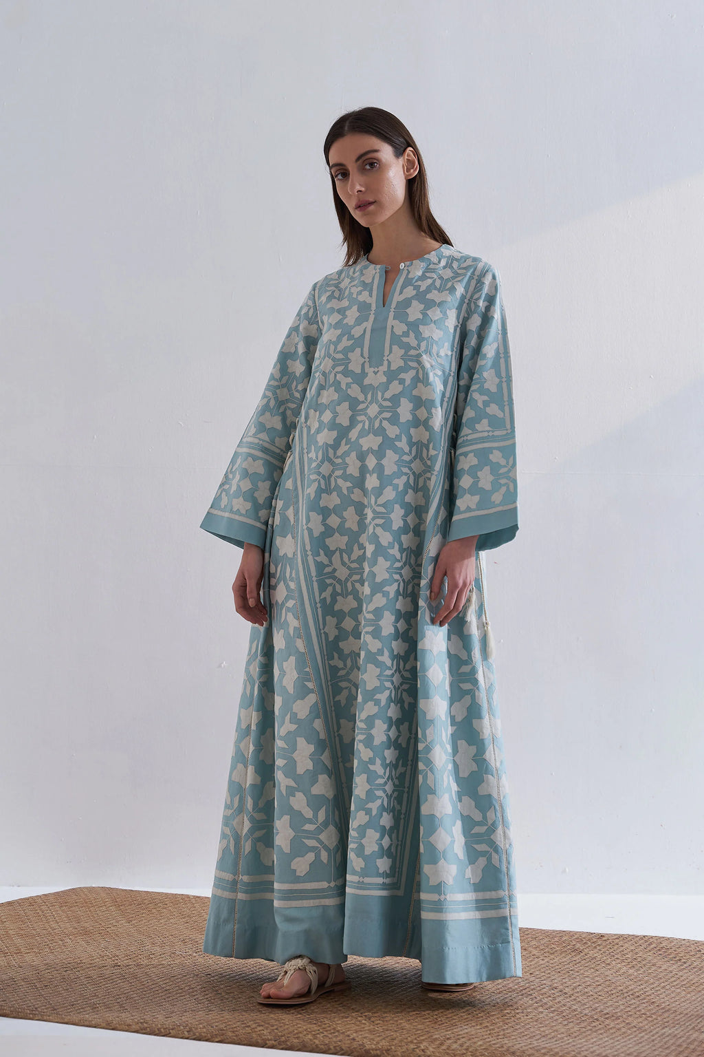 A floor-length cerulean blue Chanderi dress featuring ivory geometric hand-cut appliqué along the hemline and sleeves.