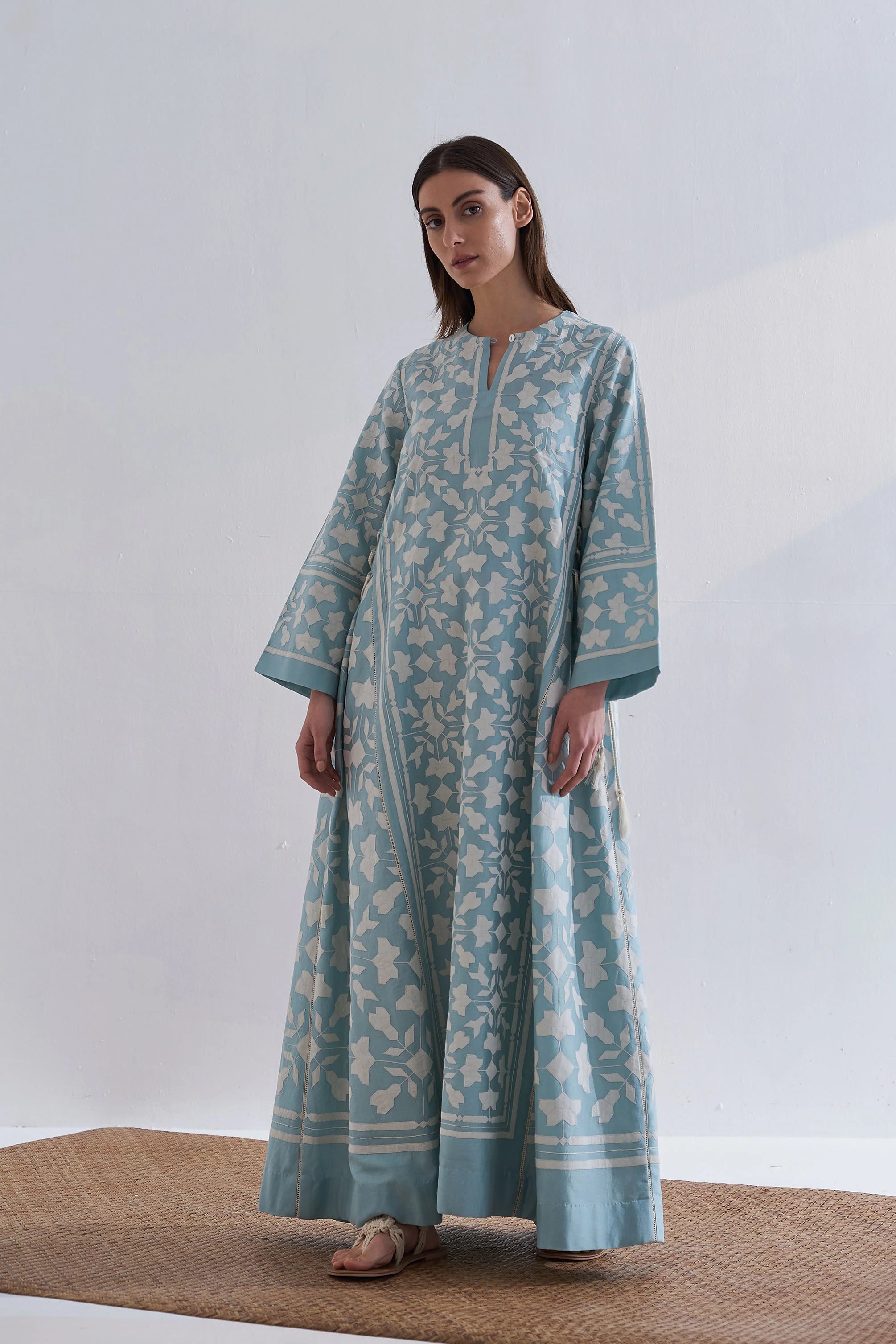 A floor-length cerulean blue Chanderi dress featuring ivory geometric hand-cut appliqué along the hemline and sleeves.