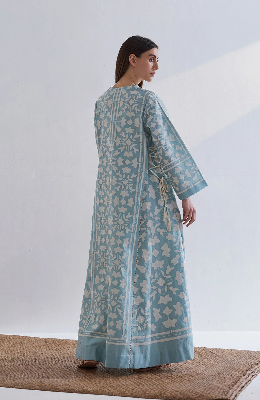 A floor-length cerulean blue Chanderi dress featuring ivory geometric hand-cut appliqué along the hemline and sleeves.