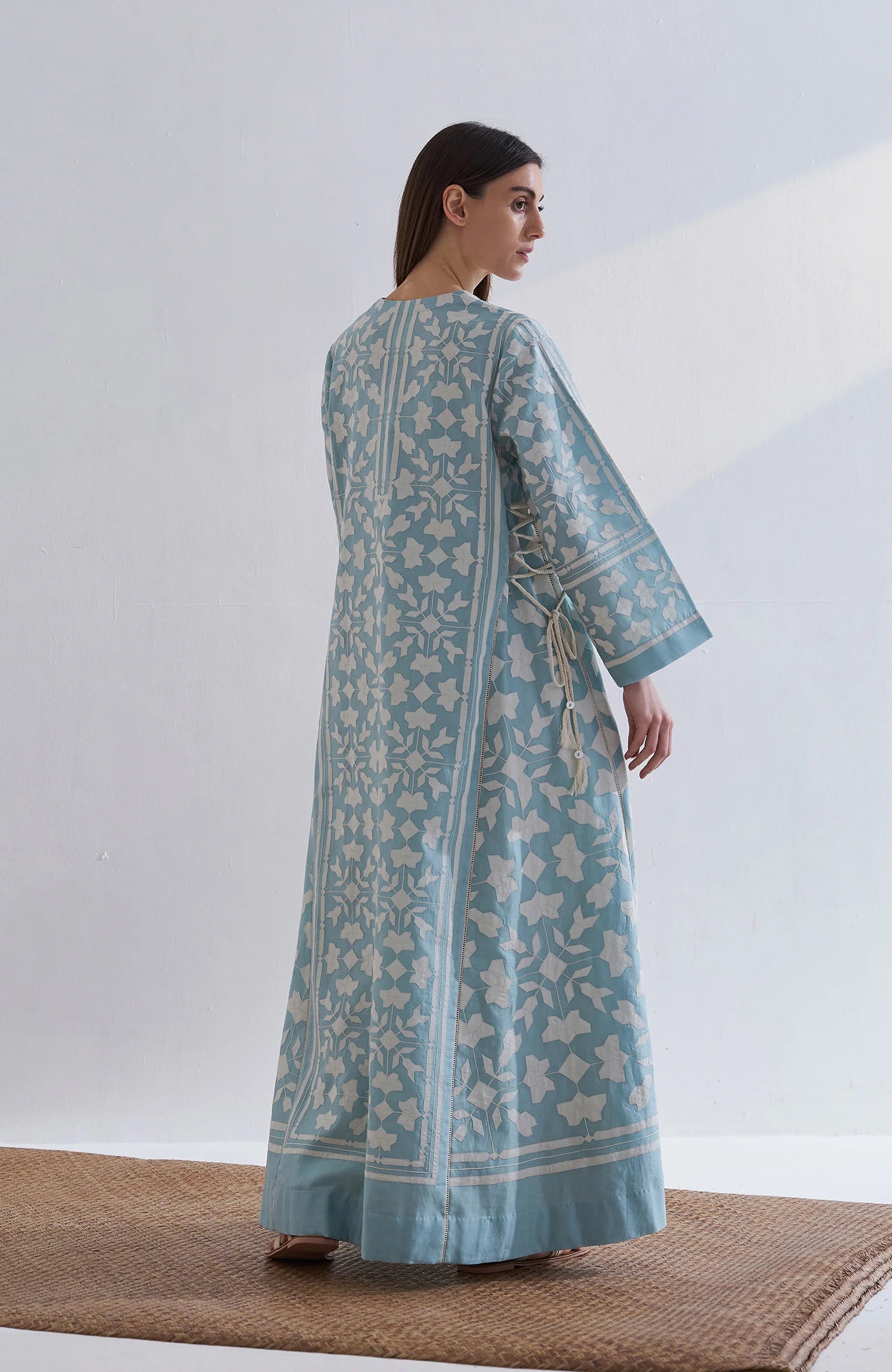 A floor-length cerulean blue Chanderi dress featuring ivory geometric hand-cut appliqué along the hemline and sleeves.