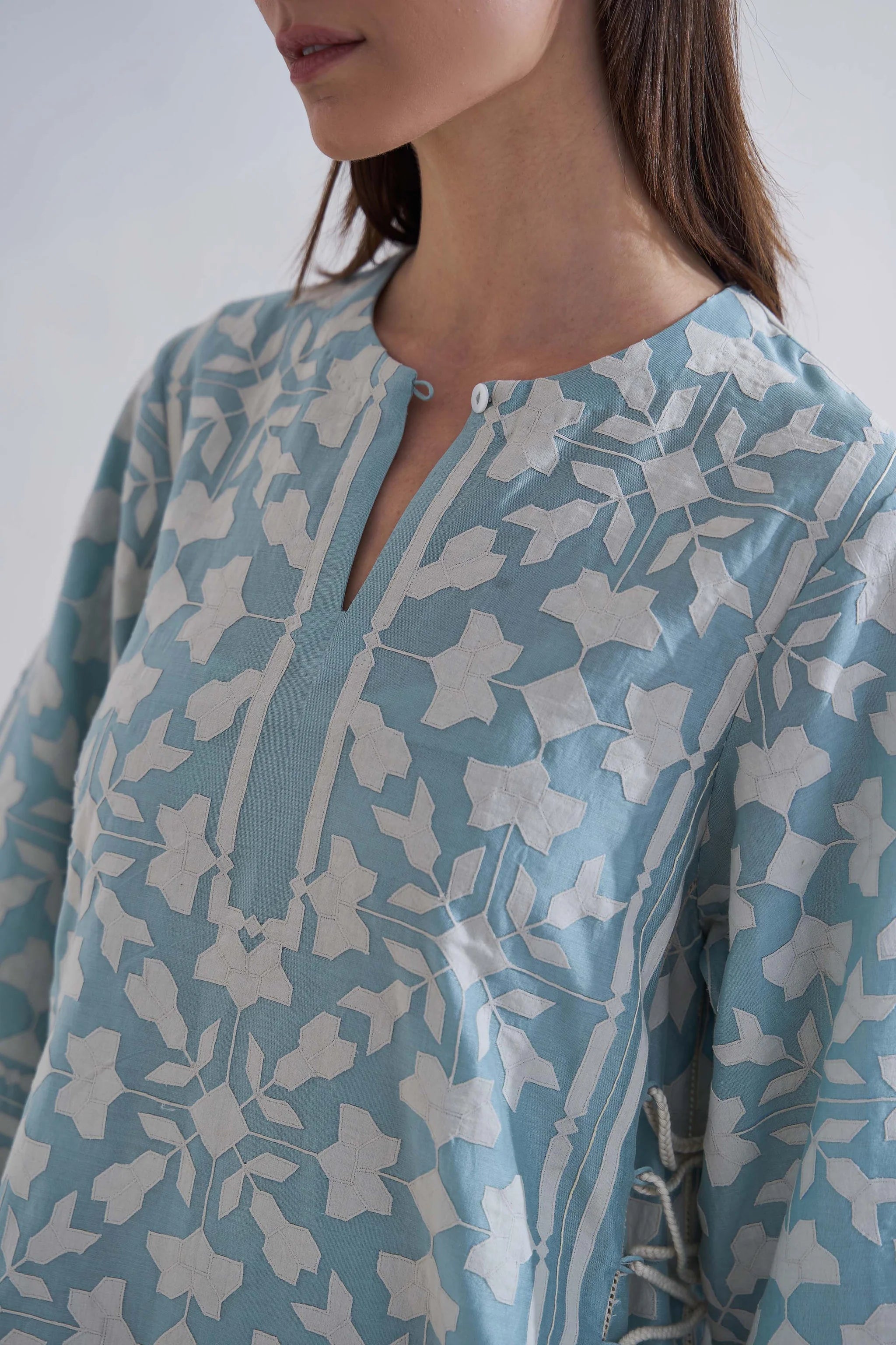 A floor-length cerulean blue Chanderi dress featuring ivory geometric hand-cut appliqué along the hemline and sleeves.