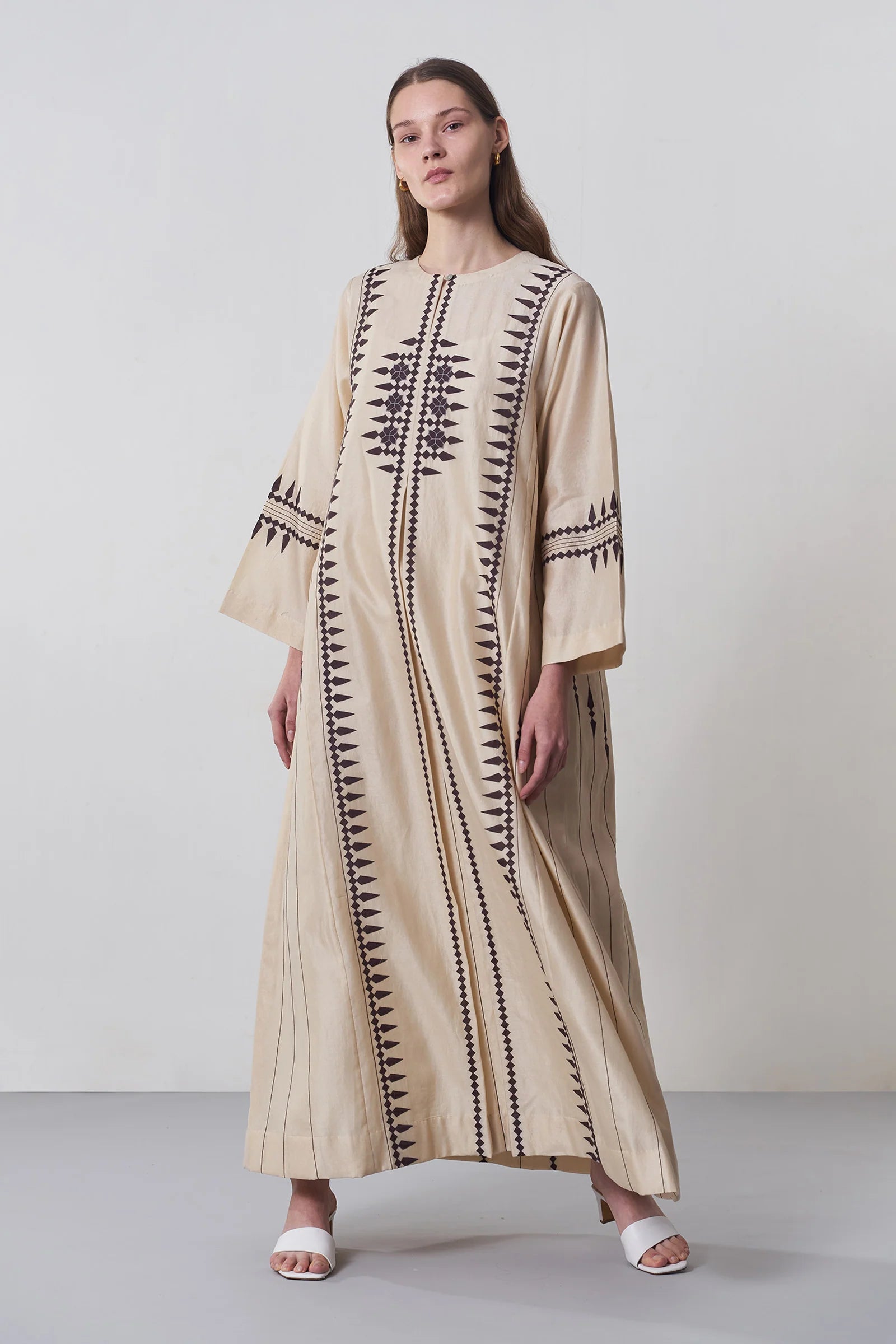 A floor-length beige Chanderi dress featuring vertical panels of ivory geometric tribal hand-cut appliqué on the bodice and hem.