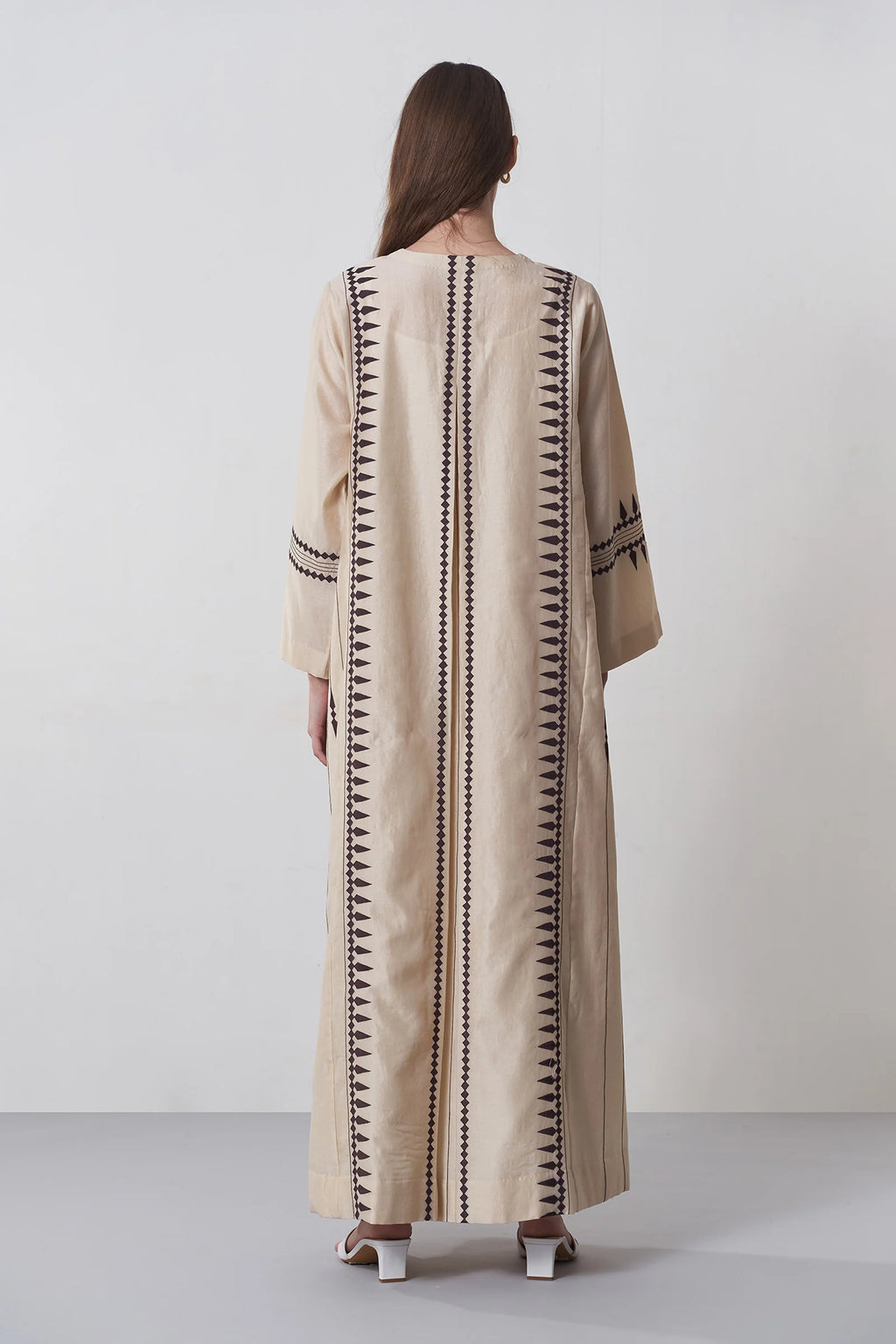 A floor-length beige Chanderi dress featuring vertical panels of ivory geometric tribal hand-cut appliqué on the bodice and hem.