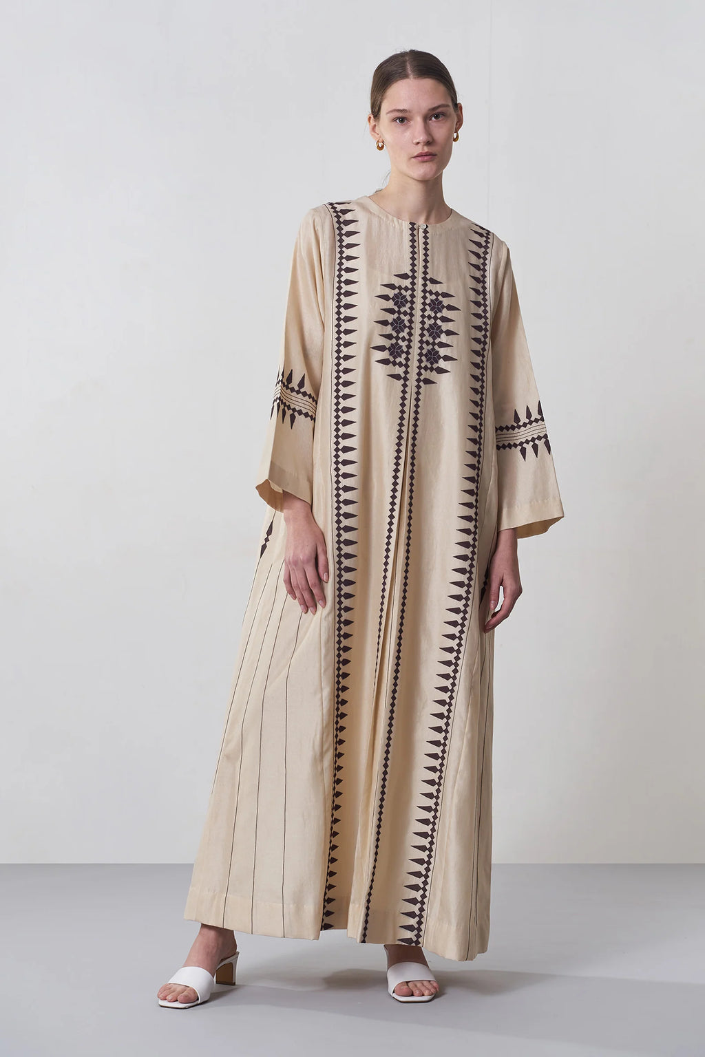A floor-length beige Chanderi dress featuring vertical panels of ivory geometric tribal hand-cut appliqué on the bodice and hem.
