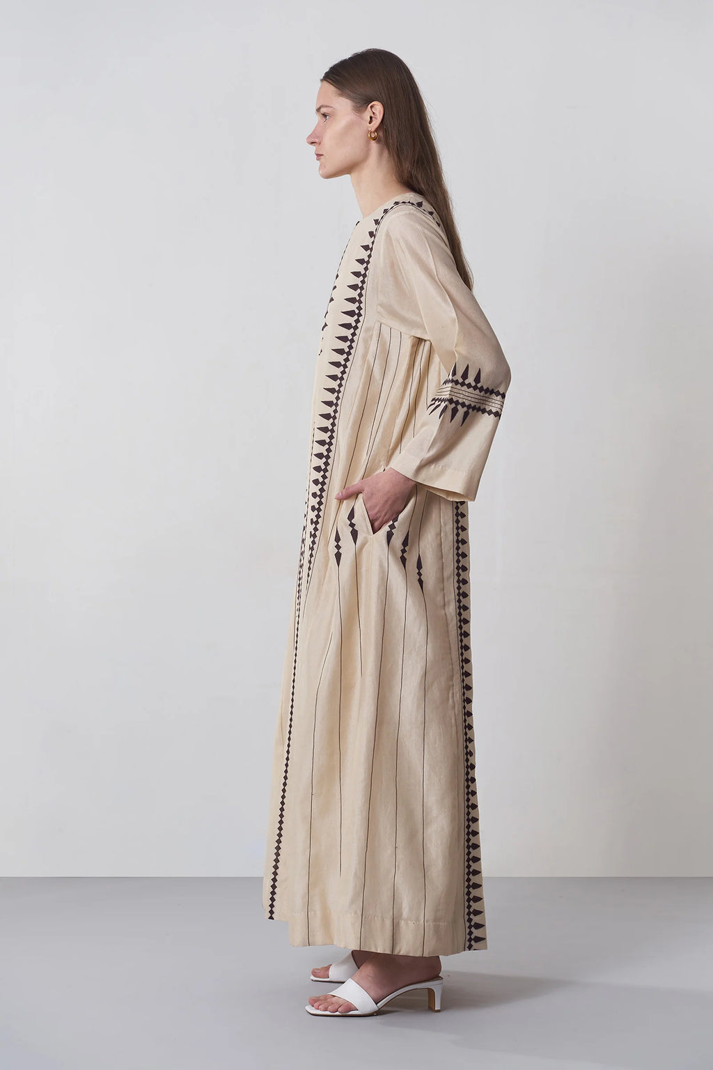 A floor-length beige Chanderi dress featuring vertical panels of ivory geometric tribal hand-cut appliqué on the bodice and hem.