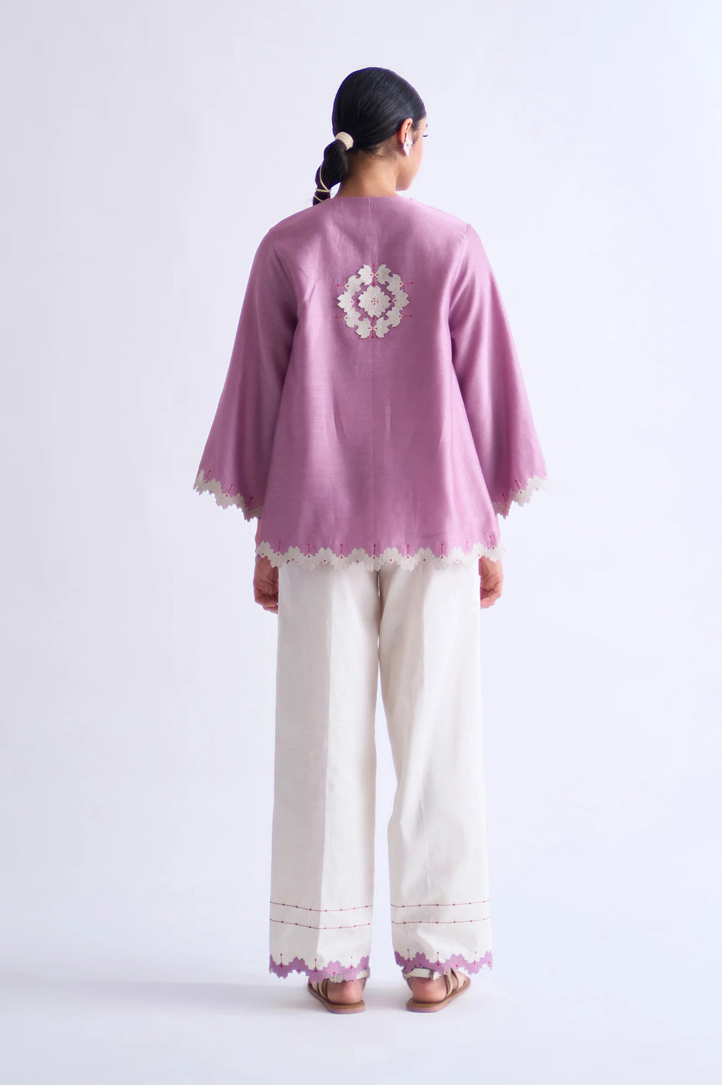A model in a blush pink A-line Chanderi shirt with ivory geometric hand-cut appliqué along the hem and sleeves, paired with matching ivory pants.