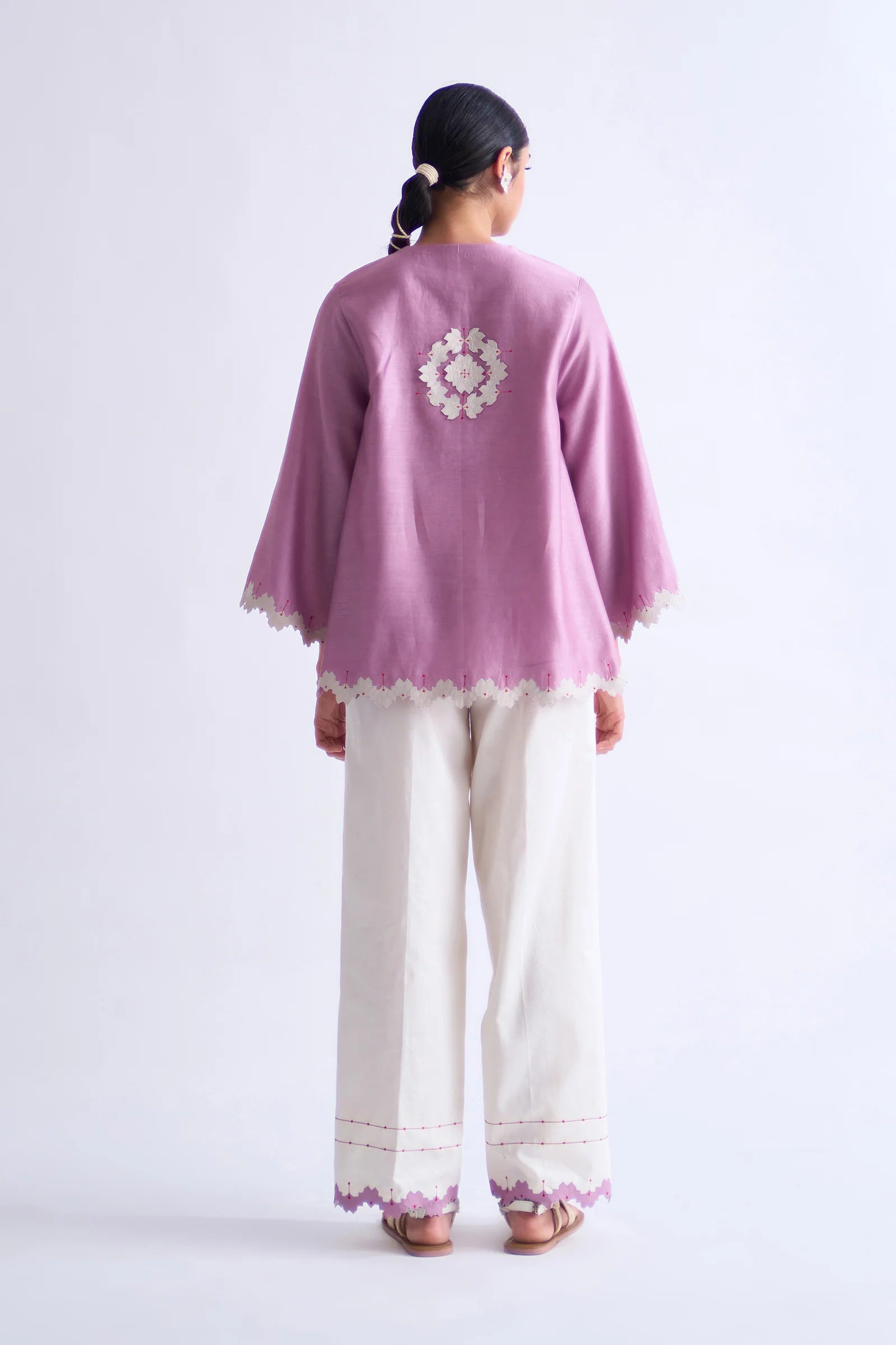 A model in a blush pink A-line Chanderi shirt with ivory geometric hand-cut appliqué along the hem and sleeves, paired with matching ivory pants.