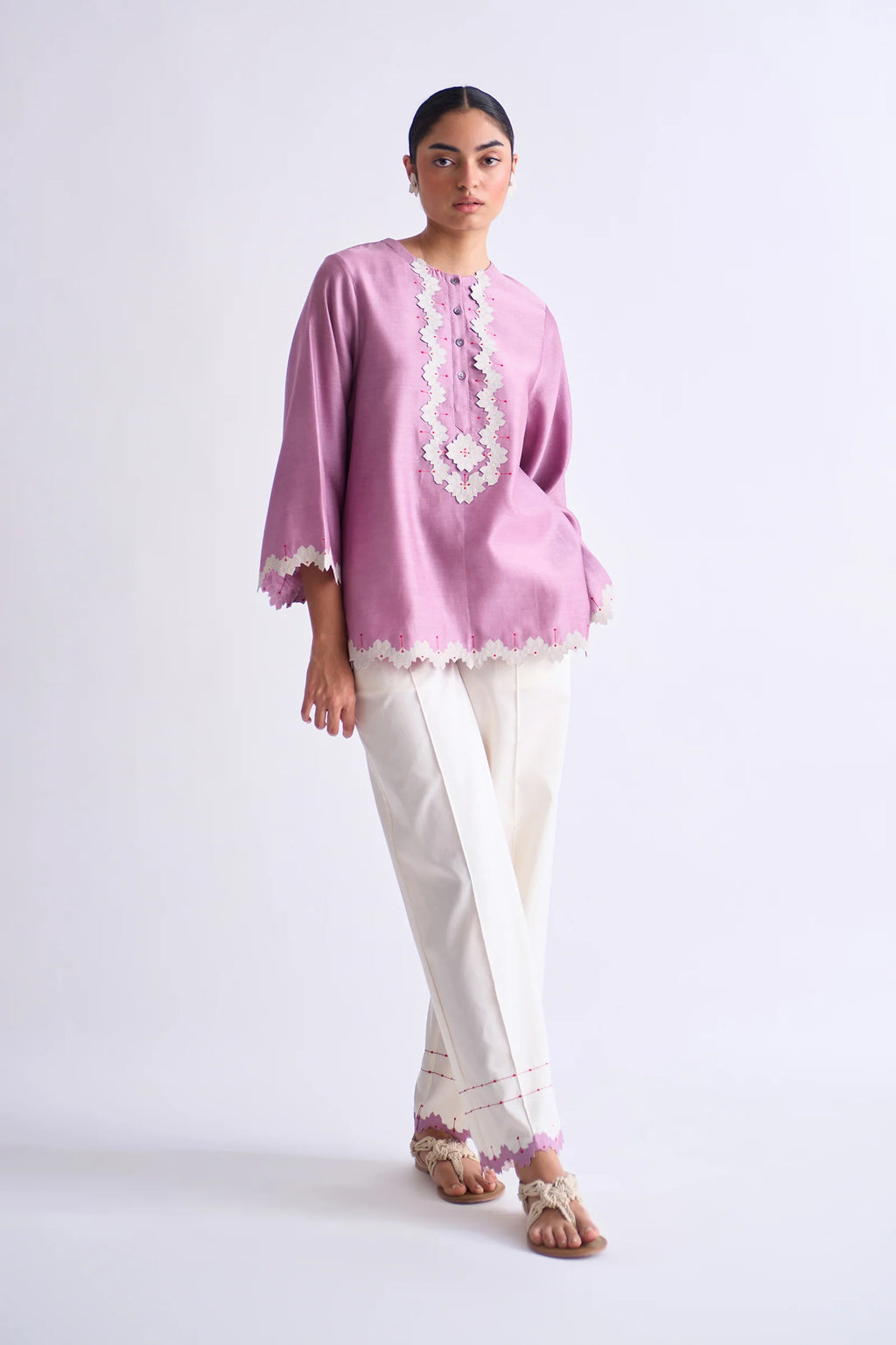 A model in a blush pink A-line Chanderi shirt with ivory geometric hand-cut appliqué along the hem and sleeves, paired with matching ivory pants.