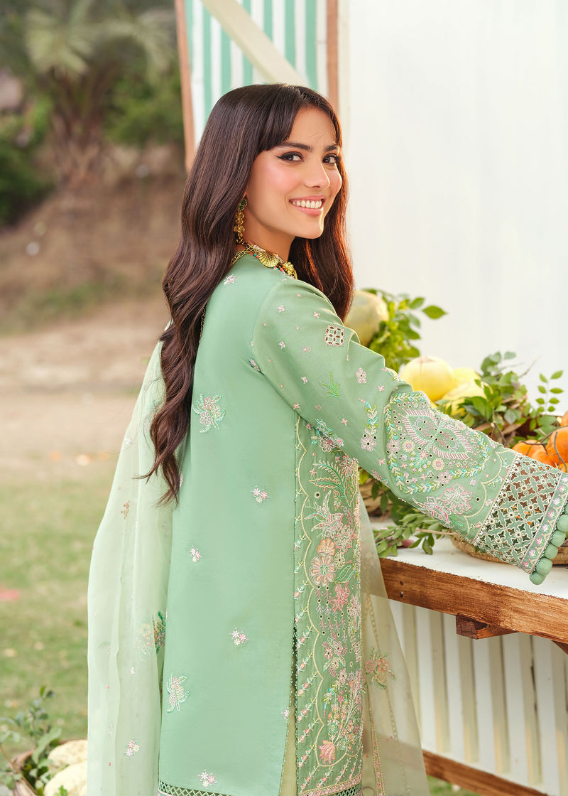 Woman in a light green embroidered outfit standing outdoors with flowers and a table in the background