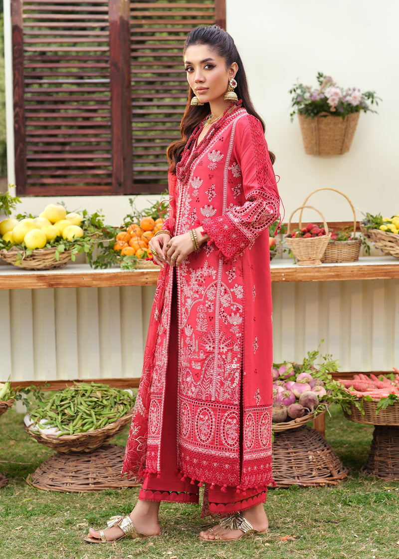 Woman in a red traditional outfit standing outdoors with a table of fruits and vegetables.