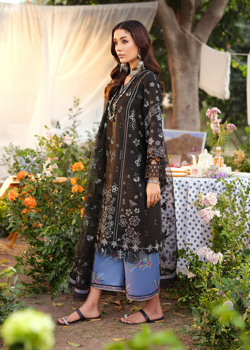 Woman in traditional black and blue outfit standing outdoors with floral decorations and a table.