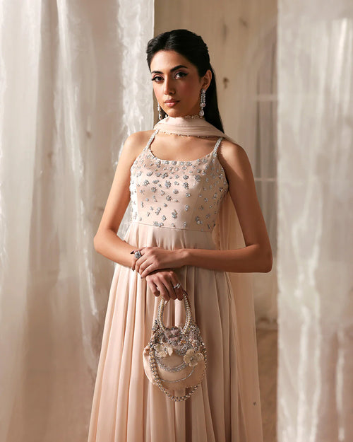 Woman in a beige dress with floral details standing against a neutral background