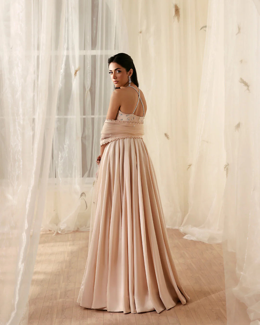 Woman in a long, flowing dress standing in front of sheer curtains.
