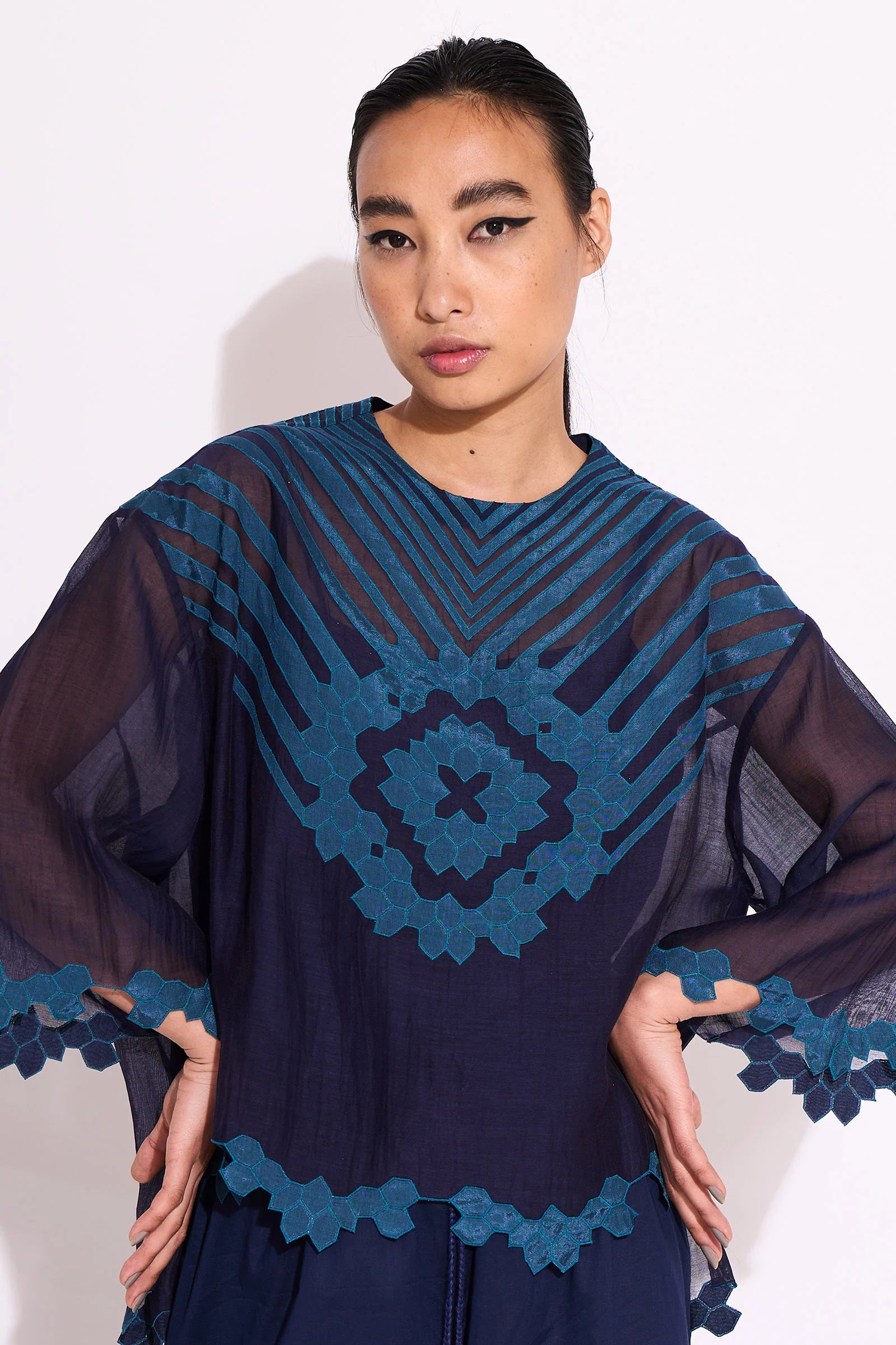 Woman wearing a dark blue dress with intricate lace details on a white background