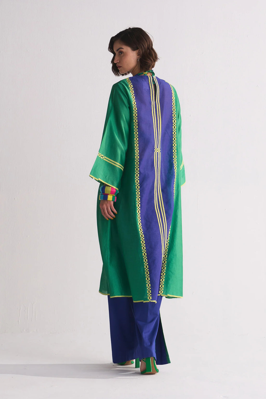 A model in a green and navy blue colour-blocked kameez featuring yellow geometric hand-cut appliqué and vertical stripe details.