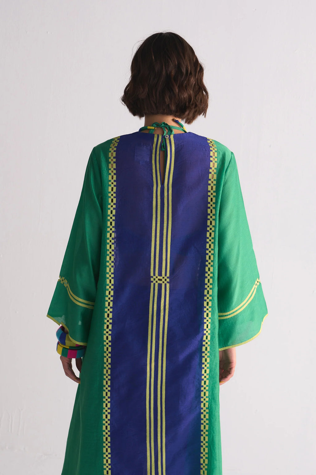 Person wearing a green and blue embroidered garment on a white background