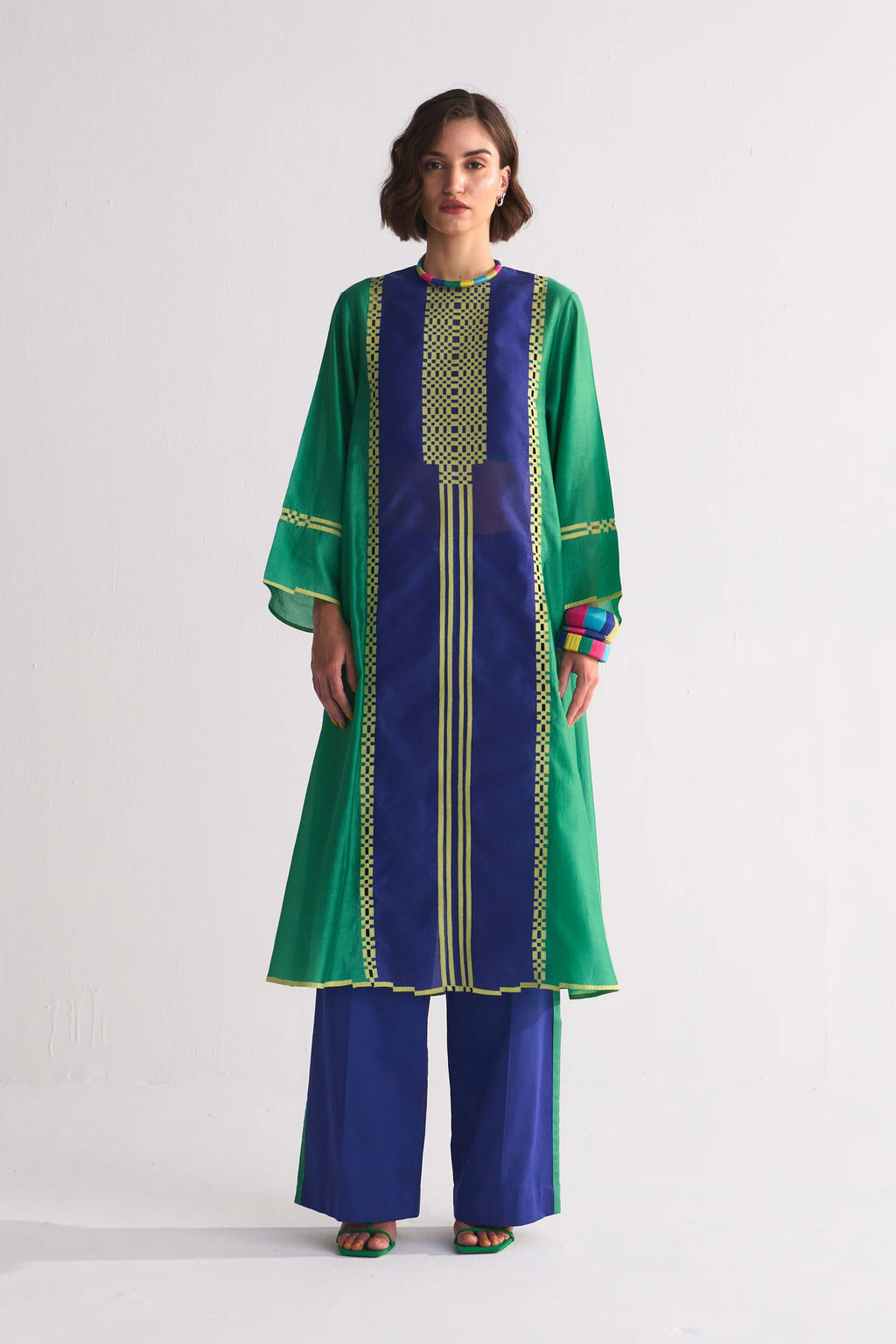 A model in a green and navy blue colour-blocked kameez featuring yellow geometric hand-cut appliqué and vertical stripe details.