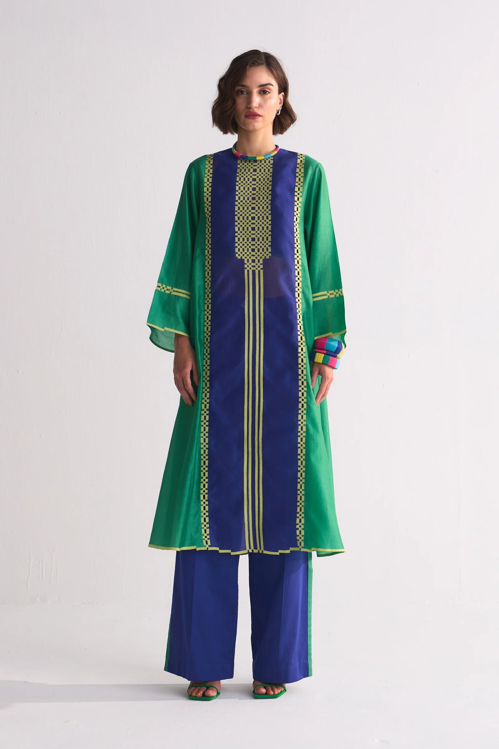 A model in a green and navy blue colour-blocked kameez featuring yellow geometric hand-cut appliqué and vertical stripe details.